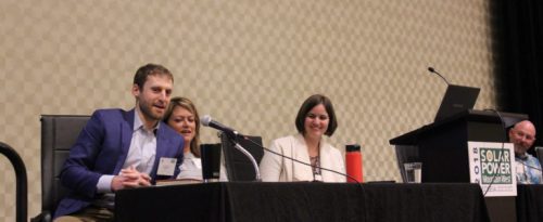 Panel discussion at a conference focusing on solar power, with three speakers seated at a table, smiling and interacting with the audience.