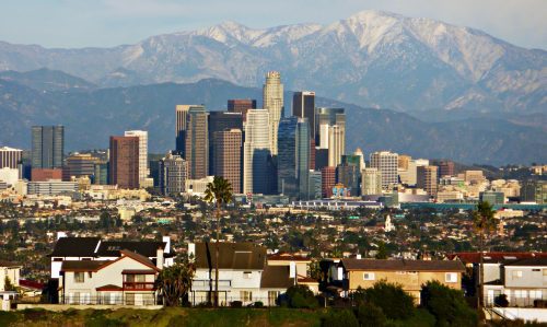 View of los angeles skyline with skyscrapers and snow-capped mountains in the background, foreground showing residential houses.