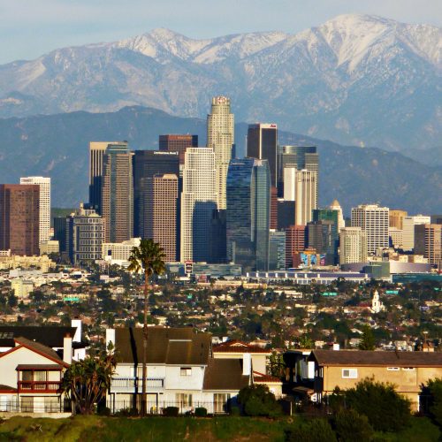 View of los angeles skyline with skyscrapers and snow-capped mountains in the background, foreground showing residential houses.