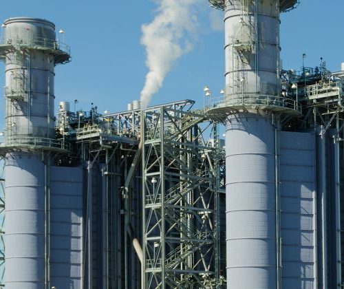 Industrial plant with tall steel towers emitting steam against a clear blue sky.