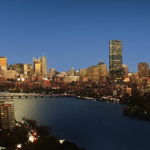 Panoramic view of boston skyline at dusk with city lights reflecting off the charles river.