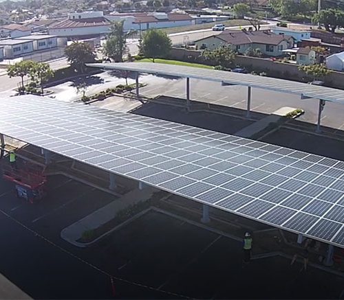Aerial view of a large solar panel installation covering a parking lot in a suburban area.