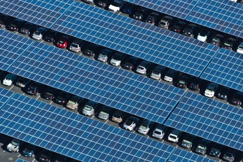 Aerial view of a parking lot covered with solar panels, with cars parked in rows between the panels.