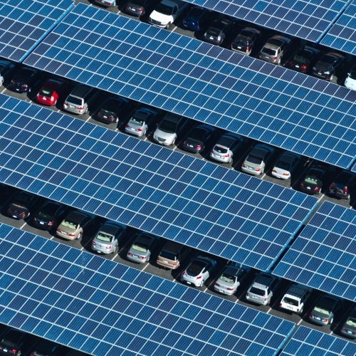 Aerial view of a parking lot covered with solar panels, with cars parked in rows between the panels.