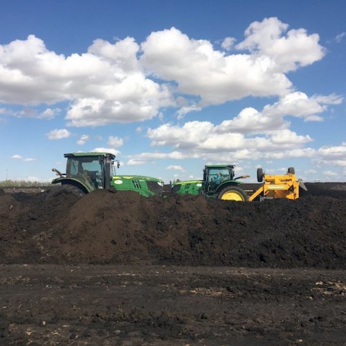 Two green tractors and one yellow bulldozer working on moving large mounds of soil in an open field under a clear sky.