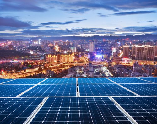 Solar panels in the foreground overlooking a brightly illuminated cityscape during twilight.