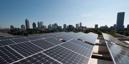 Solar panels on a rooftop with a city skyline in the background on a clear day.