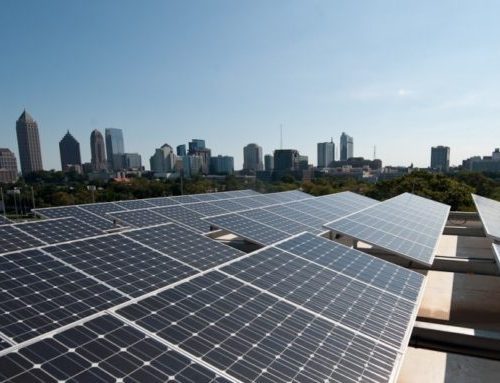 Solar panels on a rooftop with a city skyline in the background on a clear day.