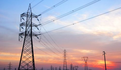 High voltage power lines and towers against a colorful sunset sky.