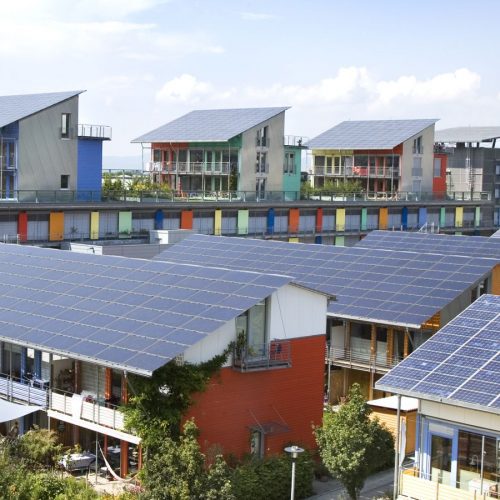 Row of modern, colorful houses with solar panels on the roofs, under a clear blue sky in an urban area.