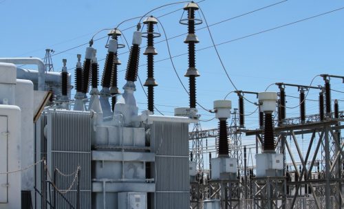 An electrical substation with transformers and high-voltage equipment under a clear blue sky.