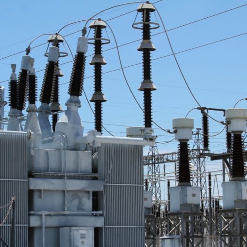 An electrical substation with transformers and high-voltage equipment under a clear blue sky.