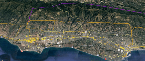 Satellite view of a coastal area with marked boundaries, showing roads, urban development, and mountainous terrain.