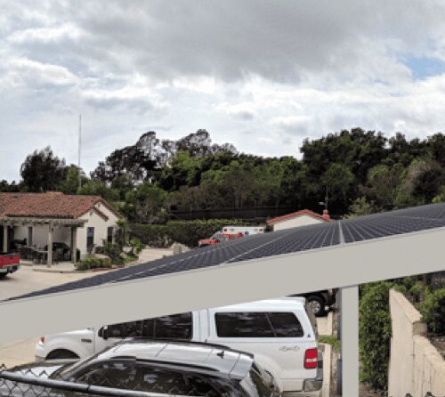 Panoramic view of a parking lot with solar panels, cars, and spanish-style buildings under a cloudy sky.