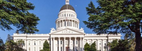 Exterior view of the california state capitol building in sacramento, framed by lush green trees under a clear blue sky.