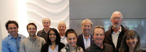 Group of nine diverse smiling professionals posing for a photo in a modern office setting.