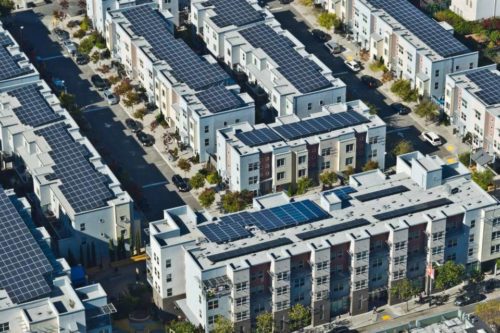 Aerial view of a residential area with rows of multi-story houses equipped with solar panels on the roofs.