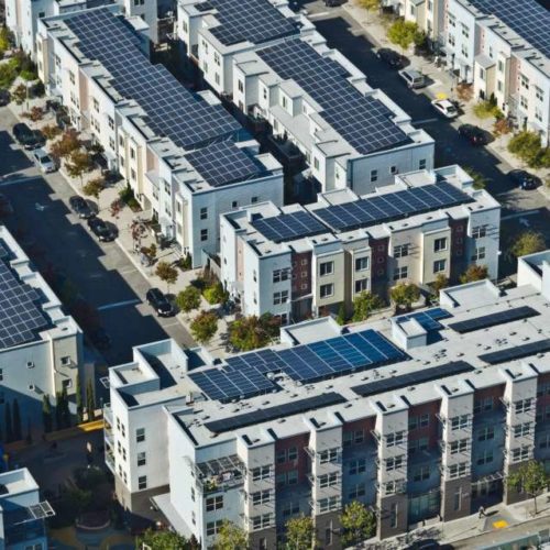 Aerial view of a residential area with rows of multi-story houses equipped with solar panels on the roofs.