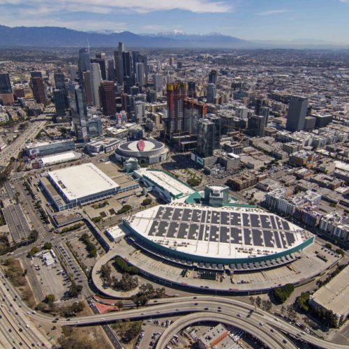 Aerial view of downtown los angeles with skyscrapers, freeways, and the distinctive architecture of the los angeles convention center visible on a clear day.