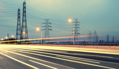 Long exposure photograph of a busy highway at dusk with streaks of light from moving vehicles and electricity pylons along the roadside.