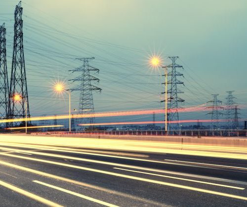 Long exposure photograph of a busy highway at dusk with streaks of light from moving vehicles and electricity pylons along the roadside.