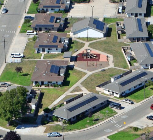 Aerial view of a suburban neighborhood with distinct houses, streets, and cars on a sunny day.