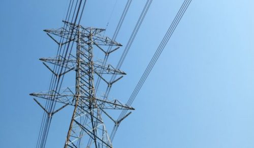 High voltage power lines suspended from a large metal tower against a clear blue sky.