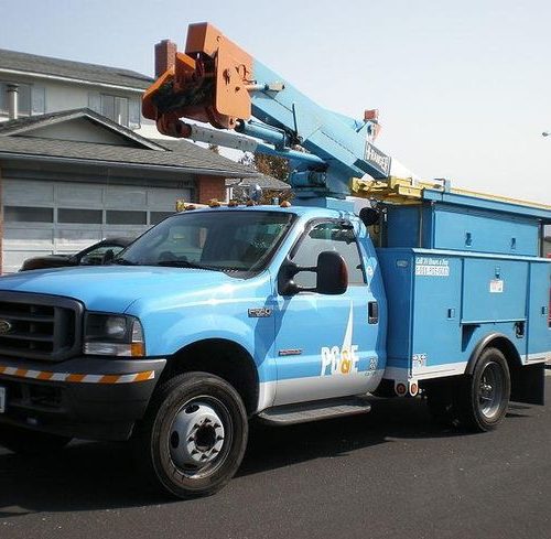 A blue utility truck with a mounted crane parked on a suburban street.