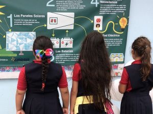 Three girls in school uniforms looking at a poster.