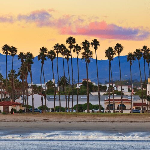 Sunset beach scene with palm trees and lighthouse.