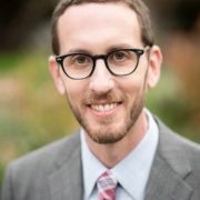 A man in glasses and suit smiling for the camera.