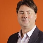 A man in a suit and tie standing next to an orange wall.