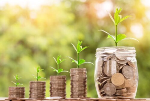 A glass jar with coins and plants growing out of it.