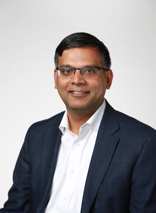 A man in a suit and glasses is smiling.