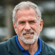 A man with grey hair and beard wearing blue shirt.