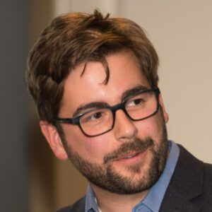 A man with glasses and beard wearing a suit.