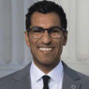 A man in glasses and suit smiling for the camera.