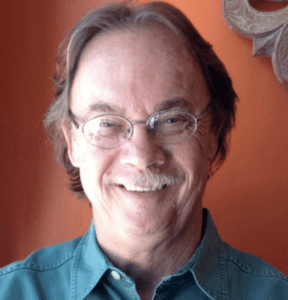 A man with glasses and long hair wearing a blue shirt.