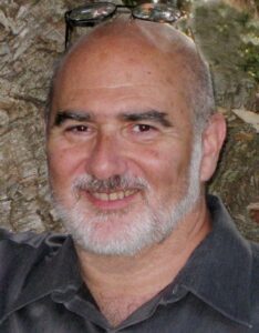 A man with grey hair and beard smiling for the camera.