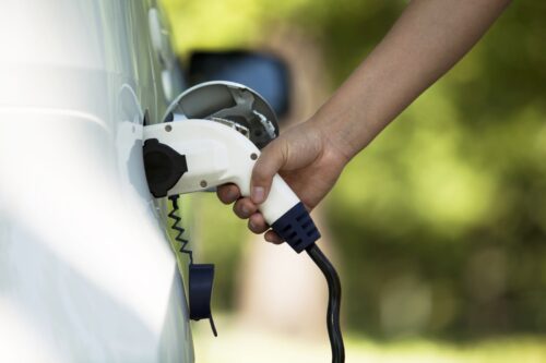 A person charging an electric car with the charger plugged in.