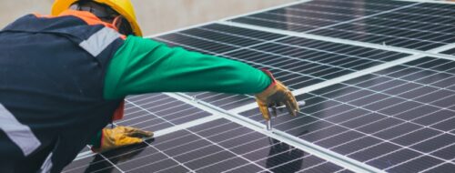 A person in green shirt and gloves on top of solar panel.