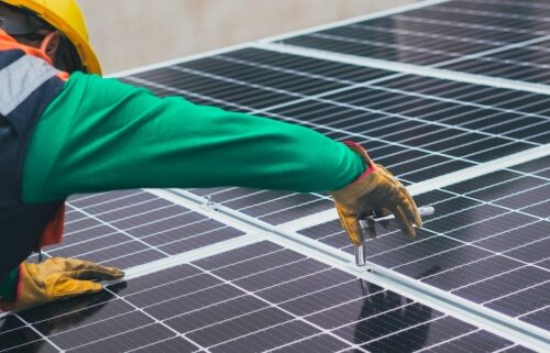 A person in green shirt and gloves on top of solar panel.