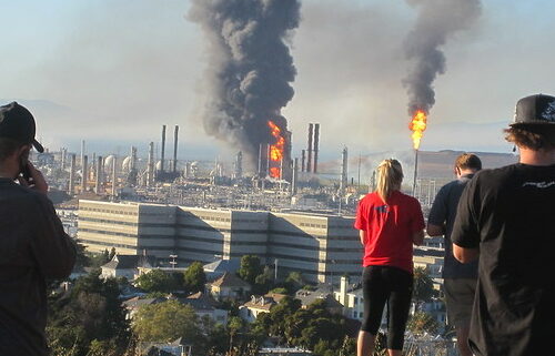 Two people standing on a hill overlooking an oil refinery.
