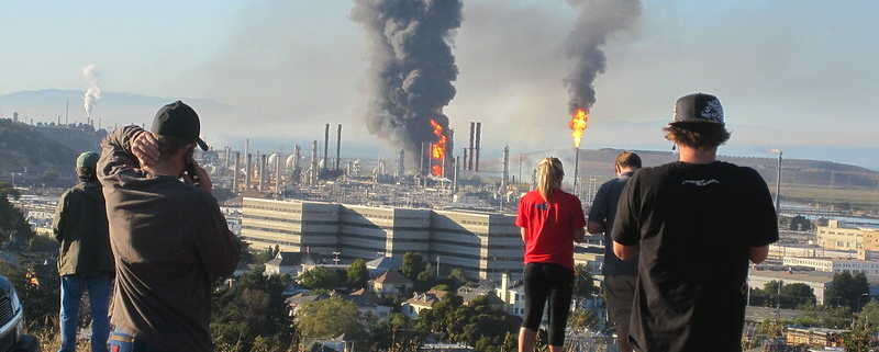 Two people standing on a hill overlooking an oil refinery.
