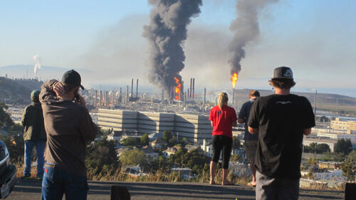 People standing on a hill overlooking an oil refinery.