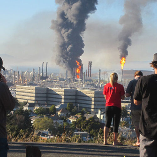 People standing on a hill overlooking an oil refinery.