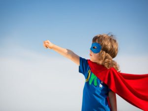 A young boy dressed as superman with his arm outstretched.