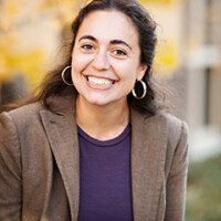 A woman in a brown jacket smiling for the camera.