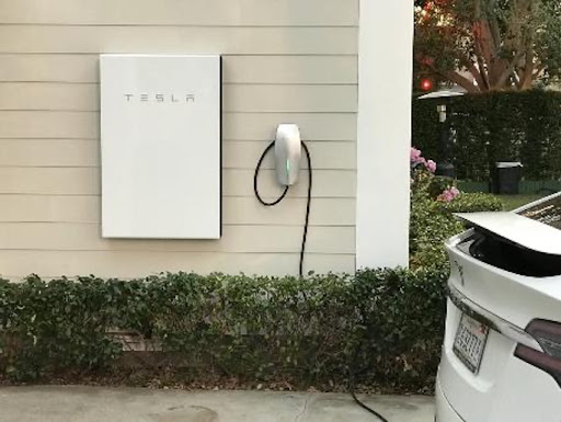 A white tesla wall mounted charger next to a house.