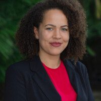 A woman with curly hair wearing a red shirt and black jacket.